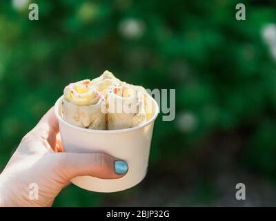 Eiscreme in der Konusschale in der Hand der Frau gerollt. Frau hält Konusbecher mit kiwi-bananen-Eiscreme im thailändischen Stil. Im Freien. Natürlicher Sommerlichtkopierraum für Text oder Design. Stockfoto