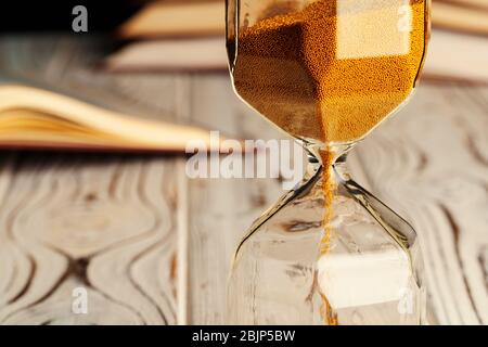 Sandglas auf Holztisch mit geöffnetem Buch aus nächster Nähe Stockfoto