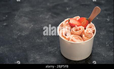 Gerolltes Eis mit Erdbeere in Kegelbecher auf dunklem rustikalem Hintergrund. Banner mit Erdbeereisten Brötchen. Gerolltes Eis im thailändischen Stil mit Kopierfläche für Text oder Design. Banner Stockfoto