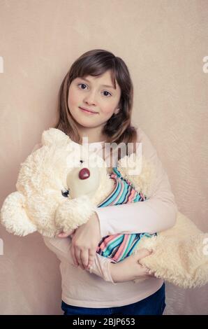 Kleines Mädchen 8 Jahre alt mit einem großen Teddybär auf rosa Hintergrund lächelnd und liebt Spielzeug ausgestopfte Tiere. Ein schönes Kind mit wunderbaren ausdrucksstarken b Stockfoto