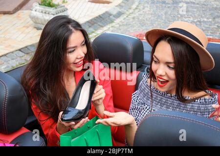Zwei schöne junge Frauen mit Einkaufstaschen im Cabrio im Freien Stockfoto