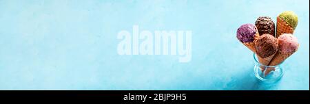 Verschiedene Eisschaufeln in Zapfen, Kopierraum. Bunte Eis in Zapfen Schokolade, Erdbeere, Heidelbeere, Pistazie oder Matcha, Kekse Schokolade Sandwich-Cookies auf blauem Hintergrund. Langes Banner Stockfoto