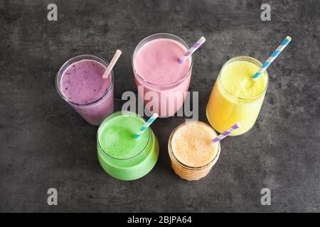 Verschiedene Fruchtmilchshakes in Glaswaren auf grauem Hintergrund Stockfoto