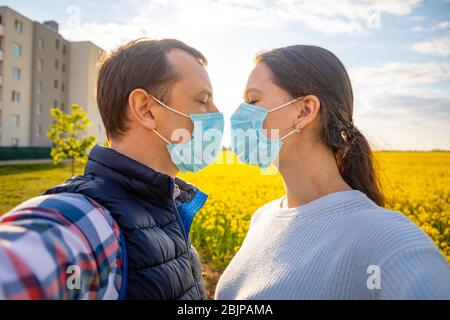 Mann und Frau küssen sich gegenseitig in schützender medizinischer Maske im Gesicht auf dem Land Stockfoto