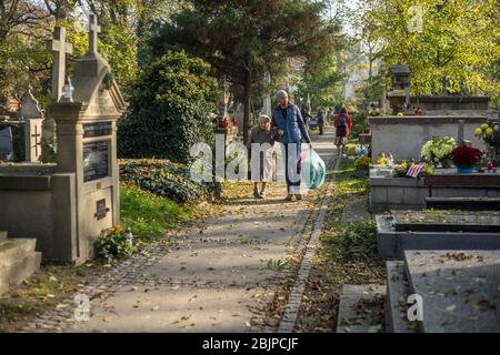 Ältere Dame und Mann, die mit Plastiktüten mit Blumen über dem Rakowicki Friedhof in Krakau, Polen 2019. Stockfoto