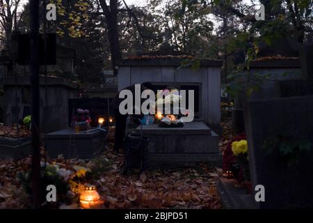 Eine ältere Frau zündet eine Kerze an einem Grab auf dem Rakowicki Friedhof in Krakau, Polen 2019 an. Stockfoto