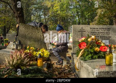 Vater und Tochter räumen ein Grab auf und stellen Kerzen und Blumen darauf auf dem Rakowicki-Friedhof in Krakau, Polen 2019. Stockfoto