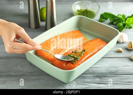 Frau bereitet Lachsfilet mit Marinade in Backform Stockfoto