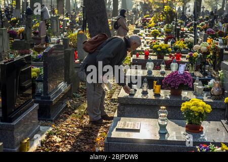 Ein Mann stellt eine Kerze auf ein Grab eines verstorbenen geliebten Menschen auf dem Rakowicki Friedhof in Krakau, Polen 2019. Stockfoto