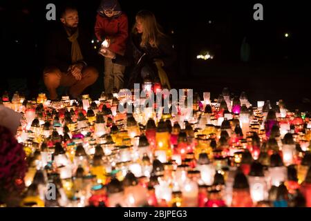 Eine junge Familie zündet vor dem Denkmal für die polnischen Opfer des Kommunismus auf dem Rakowicki-Friedhof in Krakau, Polen 2019, eine Kerze an. Stockfoto