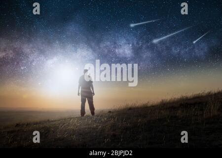 Ein Science-Fiction-Konzept. Ein Mann, der auf einem Hügel steht und über den Weltraum blickt, mit Sternschnuppen am Himmel Stockfoto