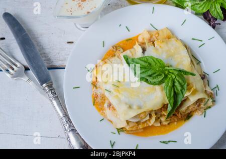 Traditionelle Lasagne mit Hackfleisch Bolognese Sauce und Bechamel Sauce mit Basilikumblättern gekrönt. Portion leckere hausgemachte Lasagne auf weißem Holz Stockfoto