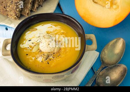 Kürbissuppe mit Sahne, Käse und Kürbiskernen auf blauem Holzhintergrund. Kürbissuppe mit frischen Kürbissen. Halloween Thanksgiving Herbst Essen Gemeinsame Lizenz Stockfoto