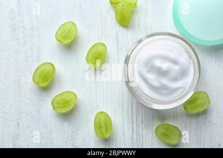 Glas mit Körpercreme und Trauben auf weißem Holzhintergrund Stockfoto