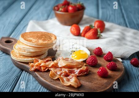 Brett mit leckeren Pfannkuchen, Himbeere, gebratenem Speck und Ei auf Holztisch Stockfoto