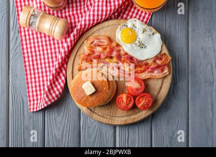 Brett mit leckeren Pfannkuchen, Tomaten, gebratenem Speck und Ei auf Holztisch Stockfoto