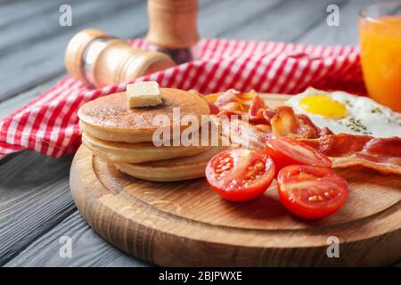 Brett mit leckeren Pfannkuchen, Tomaten, gebratenem Speck und Ei auf Holztisch Stockfoto