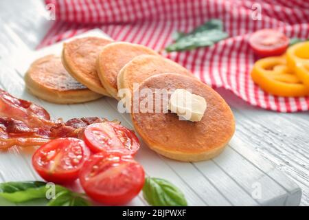 Brett mit leckeren Pfannkuchen, Tomaten und gebratenem Speck auf Holztisch Stockfoto