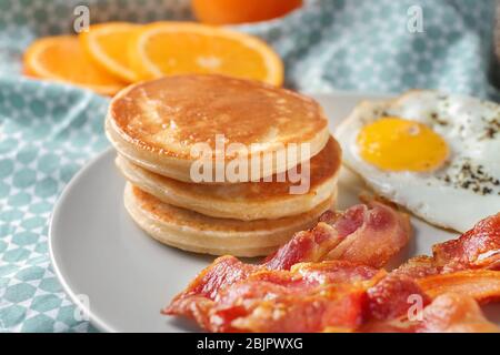 Teller mit leckeren Pfannkuchen, gebratenem Speck und Ei auf dem Tisch Stockfoto