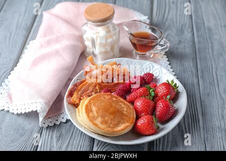 Teller mit leckeren Pfannkuchen, Erdbeere und gebratenem Speck auf Holztisch Stockfoto