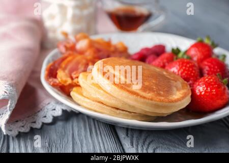 Teller mit leckeren Pfannkuchen, Erdbeere und gebratenem Speck auf Holztisch Stockfoto