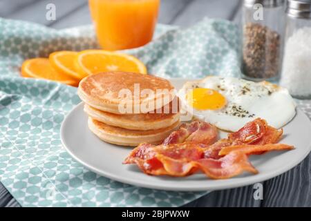 Teller mit leckeren Pfannkuchen, gebratenem Speck und Ei auf dem Tisch Stockfoto