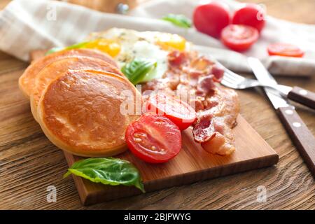 Brett mit leckeren Pfannkuchen, Tomaten und gebratenem Speck auf Holztisch Stockfoto