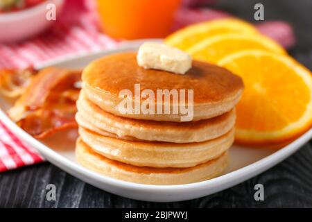 Teller mit leckeren Pfannkuchen, Orange und gebratenem Speck auf Holztisch Stockfoto