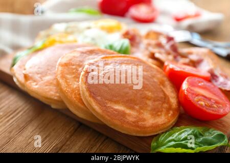 Brett mit leckeren Pfannkuchen, Tomaten und gebratenem Speck auf Holztisch Stockfoto