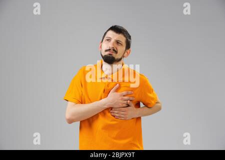 Der junge kaukasische Mann leidet unter Herzschmerz, fühlt sich krank, krank und Schwäche isoliert auf grauem Studiohintergrund. Symptome von Krankheit oder ungesunder Lebensweise. Krankheit, Unmut, traurig und verärgert. Copyspace. Stockfoto