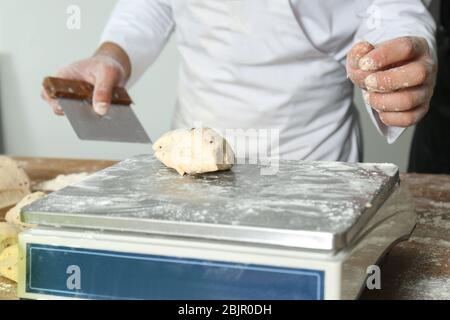 Mann wiegt rohen Teig auf Waage in der Bäckerei Stockfoto