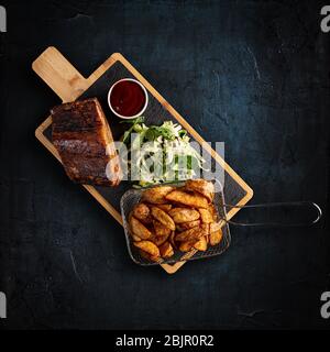 Köstliche gegrillte Rippchen serviert mit goldenen Kartoffeln und bbq-Sauce auf dunklem Hintergrund Stockfoto