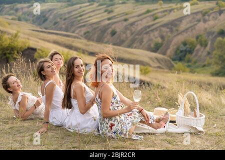 Die Firma fröhliche weibliche Freunde in weißen Kleidern mit Blick auf die grünen Hügel, entspannen Sie bei einem Picknick Stockfoto