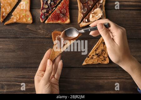 Frau verteilt Schokoladenpaste auf Toast über den Tisch Stockfoto