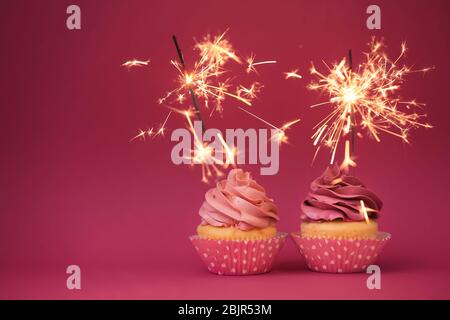 Zwei leckere Cupcakes mit Glitzern auf farbigem Hintergrund Stockfoto