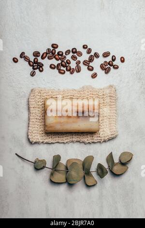 Stück Seife auf Naturbeutel mit Kaffeebohnen und Eukalyptuszweig auf rustikalem grauen Hintergrund. Gesundheits- und Schönheitskonzept. Stockfoto