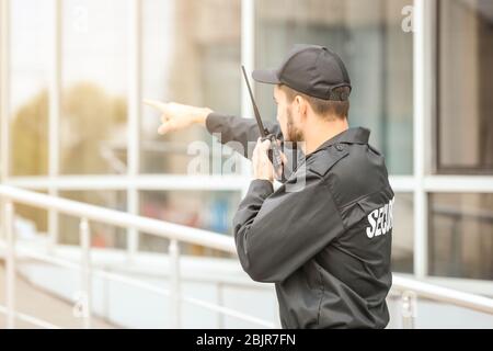 Männlicher Wachmann mit tragbarem Funksender in der Nähe des Gebäudes im Freien Stockfoto