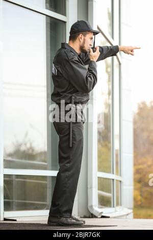 Männlicher Wachmann mit tragbarem Funksender in der Nähe des Gebäudes im Freien Stockfoto