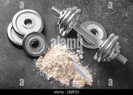 Haufen von Protein-Pulver mit Schaufel, Hantel und Scheiben auf dem Tisch Stockfoto