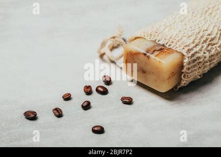 Stück Seife in Naturbeutel mit Kaffeebohnen auf rustikalem grauen Hintergrund. Gesundheits- und Schönheitskonzept. Stockfoto