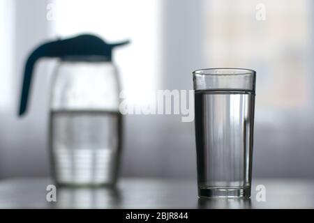 Ein Glas mit Wasser und eine Karaffe im grauen Hintergrund Stockfoto