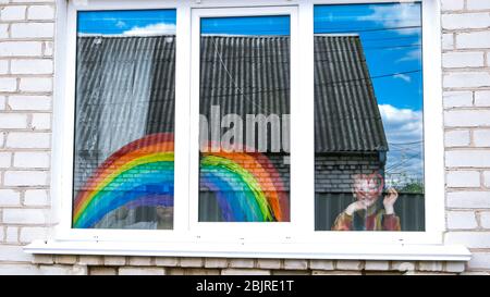 Junge am Fenster, Regenbogen. Ende der Quarantäne. Ein Junge zeichnet ein Regenbogen und ein rotes Herz. Das Konzept der Verfolgung des Regenbogens. Lasst uns alle gut sein Stockfoto