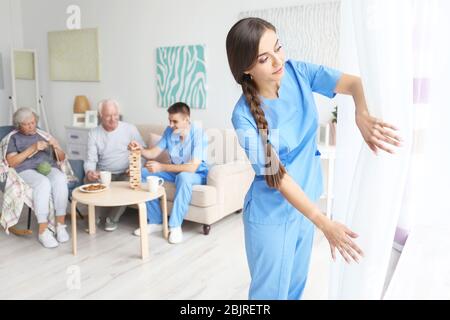 Junge Frau in uniform öffnenden Vorhängen im Innenbereich Stockfoto