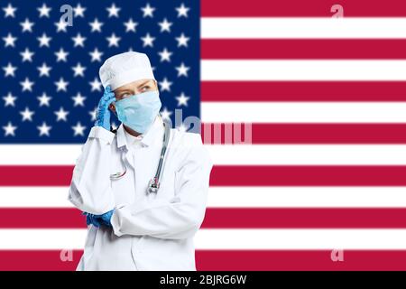 Junge Ärztin mit Stethoskop und Gesichtsmaske, die für Gott betet, mit US-Nationalflagge auf Hintergrund. Konzept der Medizin und Gesundheit, Coronavirus Pandemie, Gefahr Epidemie, COVID. Stockfoto