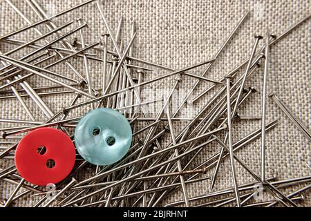 Roter und blauer Knopf mit Schneidernadeln auf Sackkleidung. Nahaufnahme. Stockfoto