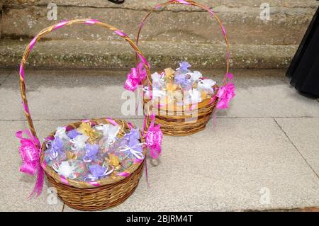 Gefärbter Reis in Organza-Tütchen in einem Weidenkorb mit einem weiteren Korb hinter bereit, um auf eine Feier zu werfen. Stockfoto
