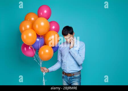 kaukasischer Mann im Hemd mit hellen bunten Ballons denken über somethinh isoliert auf blauem Hintergrund. Stockfoto