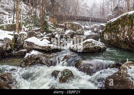 Eine verschneite, winterliche Szene umhüllt das kristallklare blaue Wasser, das um die massiven Felsbrocken fließt, die die Länge von Wolf Creek in der New River Gorge definieren Stockfoto