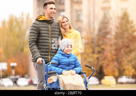 Pärchen mit ihrem kleinen Sohn im Rollstuhl draußen am Herbsttag Stockfoto