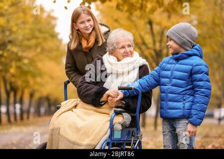 Nette Kinder mit ihrer älteren Großmutter im Rollstuhl im Freien am Herbsttag Stockfoto